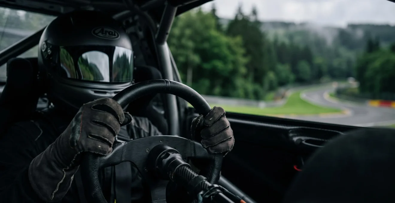Casque de course et mains gantées sur un volant, symbolisant l'évaluation du talent pur d'un pilote au-delà de sa machine