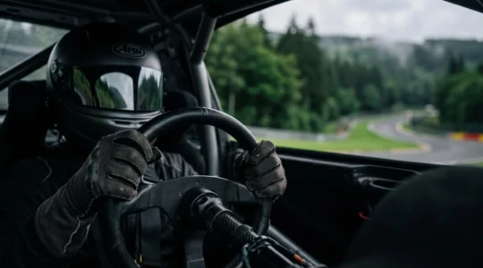 Casque de course et mains gantées sur un volant, symbolisant l'évaluation du talent pur d'un pilote au-delà de sa machine