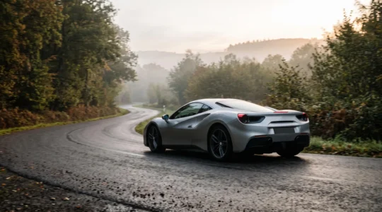 Voiture de sport vue de trois-quarts arrière s'engageant dans un virage sur une route sinueuse des Ardennes belges au lever du jour